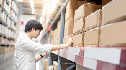 Young Asian shopper man picking cardboard box package from product shelf in warehouse. Male...