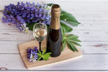 a bottle of champagne with a glass. Flowers on the background of a wooden Board with an alcoholic drink.