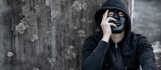 Mystery man in black mask with hoodie jacket sitting on abandoned building feeling tired and...