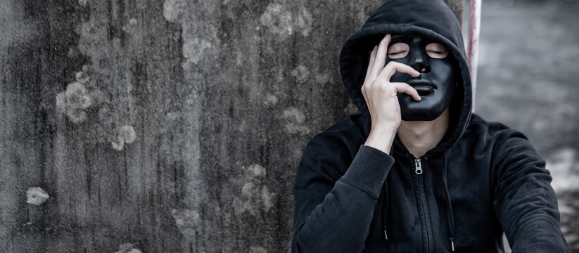 Mystery man in black mask with hoodie jacket sitting on abandoned building feeling tired and stressed. Depression (Major depressive disorder) or mental health problem concepts.