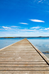 Obraz premium Wooden bridge extending to horizon with ocean and blue sky with clouds