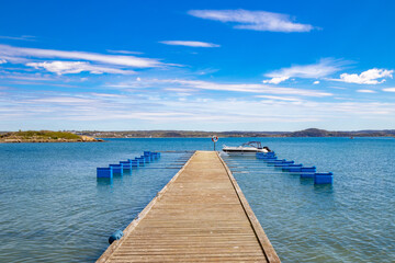 Jetty with boat against blue sky and distant coastline