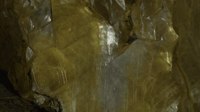 Closeup view of a massive chunk of an yellow crystal located in a dark cave.