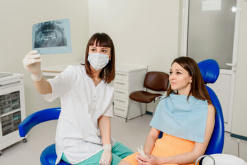 Fototapeta na wymiar Young woman dentist explaining to her patient on a dental x-ray panoramic radiography all the dental treatment that needs to do in dentistry