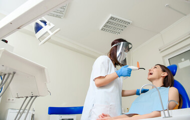 Obraz premium The dentist is using the photopolymer light for finishing the dental filling treatment in dentistry.