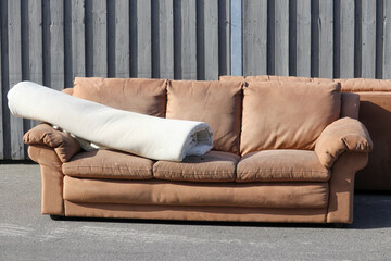 A sofa and a carpet left on pavement as trash