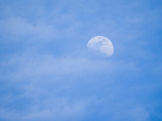 Naklejka na ściany i meble Looking up into a blue sky with an illuminated moon during the daylight hours