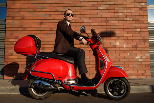 Street photo concept of a young elegant man in classic suit on a red vintage motorbike scooter