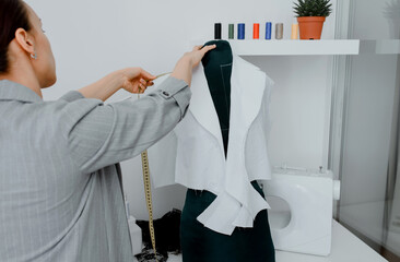 Young woman tailor is measuring with a centimeter ribbon a future shirt