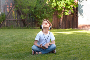 Naklejka na ściany i meble a boy in a T-shirt sits on the green grass and listens to music on headphones