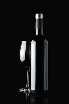 Glass of red wine next to a bottle isolated on black background