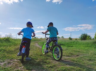 two little boys learn to ride bikes in the field on a sunny day