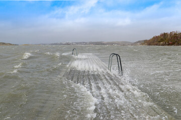 Waves rolling over a bridge with swimming ladders in a storm in Sweden