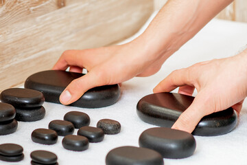 Hands of massage therapists taking black hot massage stones from set on the table in spa.