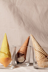 Various ice cream waffle cone in glass on beige pastel background.Fashion food composition
