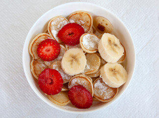 Tasty trendy breakfast - mini cereal pancakes with strawberry, banana and sugar powder.
