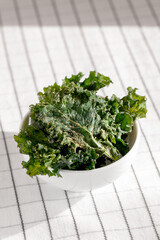 Close-up of white ceramic bowl full of healthy veggie chips made of kale with pepper and olive oil.Low-carb and gluten free vegetable crisps snack