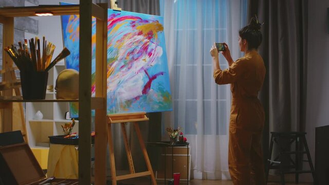 Successful woman painter making a photo of her masterpiece on canvas in art studio. Modern artwork paint on canvas, creative, contemporary and successful fine art artist drawing masterpiece