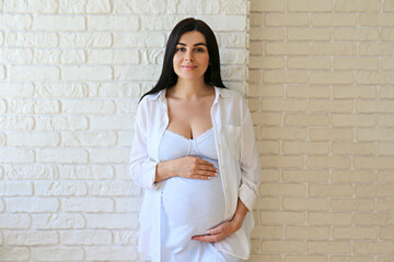 Portrait shot of young beautiful woman on third trimester of pregnancy. Close up of pregnant female with arms on her round belly. Expecting a child concept. Background, copy space.