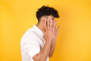 Portrait of young man with shocked facial expression, holding hands near face, screaming and looking sideways at something amazing. Stands against gray studio Wall.