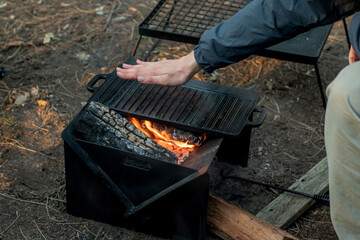 Setting the campfire in a portable foladble firepit for a camp cooking on cast iron plate.