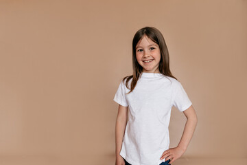 Obraz premium Confident smiling little girl in white t-shirt looking at camera on isolated background. Indoor portrait of pretty lovely girl