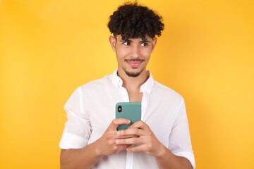 Horizontal shot of pretty young male with afro hair looks with bugged eyes, holds modern smart phone, receives unexpected message from friend, reads reminder, isolated over yellow background.