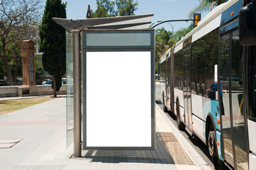 White blank vertical billboard at the bus stop on the city street. In the background of buses and...