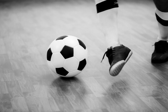 Black and white image of Futsal ball with motion blurry futsal player run and contol ball to shoot  to goal on wooden floor in sports hall. Youth futsal league. Soccer game indoor.