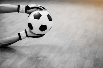 Black and white image of ball in hands of futsal goalkeeper on wooden futsal floor. Indoor soccer...