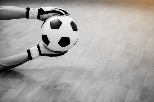 Black and white image of ball in hands of futsal goalkeeper on wooden futsal floor. Indoor soccer sports hall. Football futsal player, ball, Sports background. Youth futsal league.