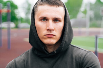 Portrait of a sportsman in a black hooded suit against the backdrop of a sports field