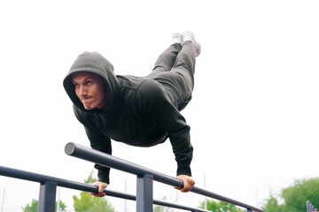 Athletic man young fitness trainer doing pushups on bars at a playground in a stadium