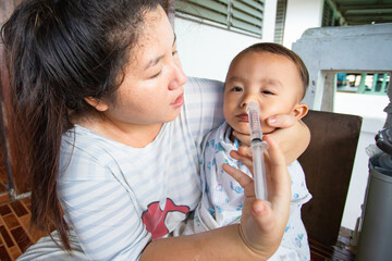 Asian mom cleaning her son's nose with a syringe