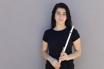 Black-haired girl holds the flute outside in front of a grey background