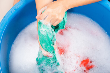 Fototapeta premium Closeup young Asian woman use hands washing color clothes in basin with detergent have soapy bubble water, studio shot background, laundry concept