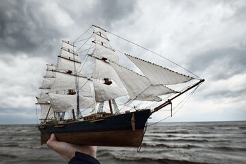 Antiquarian wooden scale model of the clipper tall ship, close-up. Dramatic sky and sea shore in the background. Traditional craft, souvenirs, hobby, collecting, vintage, modeling. Zero waste concept © Alex Stemmer