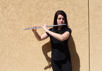 Black-haired girl plays the flute outside in front of a wall © Joahim