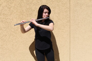 Black-haired girl plays the flute outside in front of a wall © Joahim