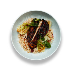 A delicious bowl of Jerk chicken, rice and vegetables, in a light blue bowl isolated on white