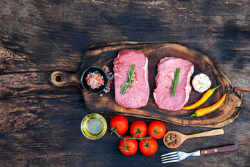 Raw meat beef steak organic fresh ingredient on wooden board table background in kitchen with rosemary, salt, garlic, tomato, black pepper, olive oil. Meat beef on wooden plate for beefsteak raw meat