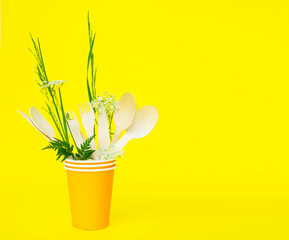 disposable wooden forks, spoons and knives in a paper cup on yellow background. eco friendly. no environmental pollution, no plastic.
