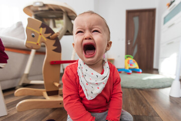 Little girl sitting on the floor at home and crying. One year old baby crying