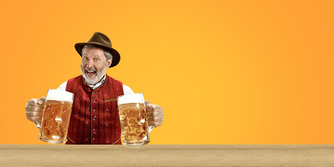Delighted senior man with beer dressed in traditional Austrian or Bavarian costume holding mug of...