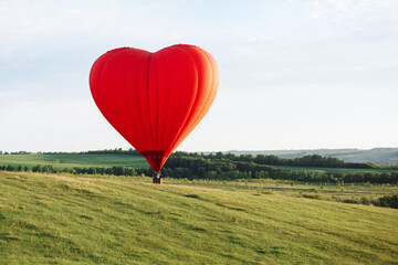 Naklejka premium Hot air balloon in shape of heart is landing on the green field