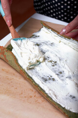 A woman puts cream on cake to prepare a biscuit roll with spinach and mint. Stuffed with strawberries. Ingredients for cooking.