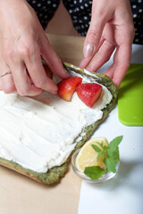 Cream on the cake for the preparation of biscuit roll with spinach and mint. A woman puts strawberry filling on it. Ingredients for cooking.