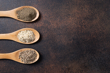 Hemp seeds, flour, kernels in spoons on dark background. View from above.