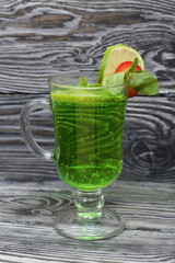 Green lemonade in a glass. Decorated with lime and strawberries. With sprigs of mint. On pine boards.
