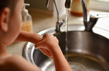 The child washes his hands in the house. Water tap for washing hands.
